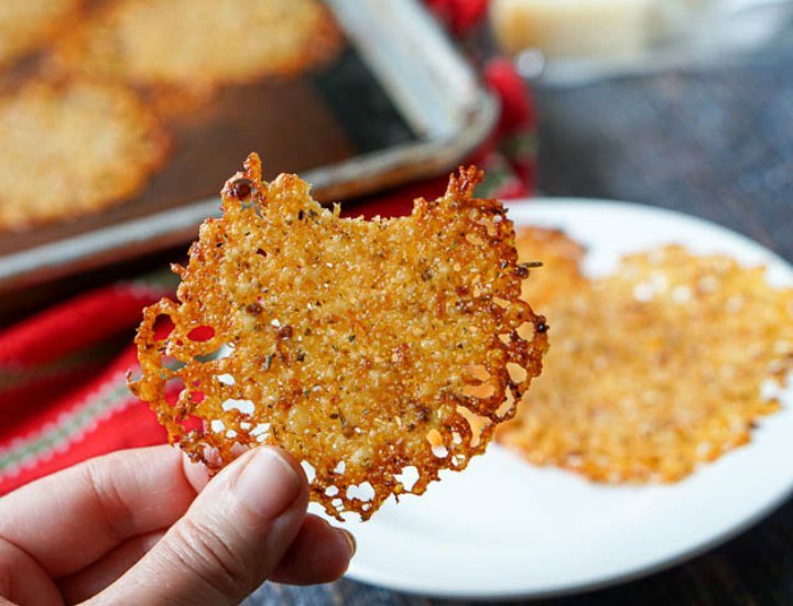 hand holding a keto parmesan cheese crisp with a bite taken out and a white plate in background