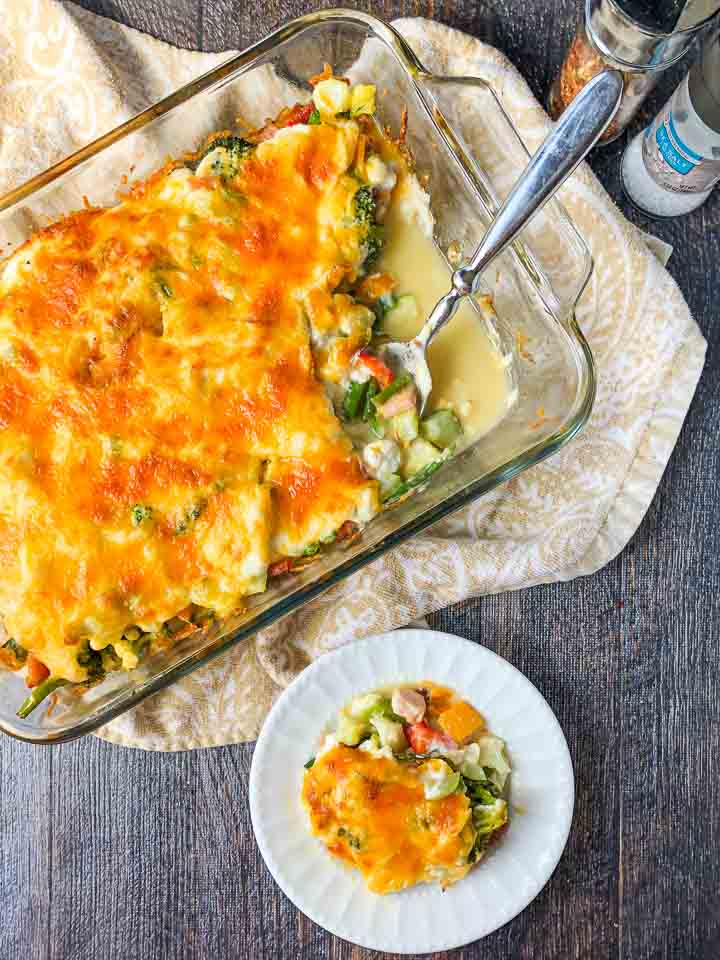 white plate and baking dish with low carb creamy vegetable & ham casserole and silver spoon