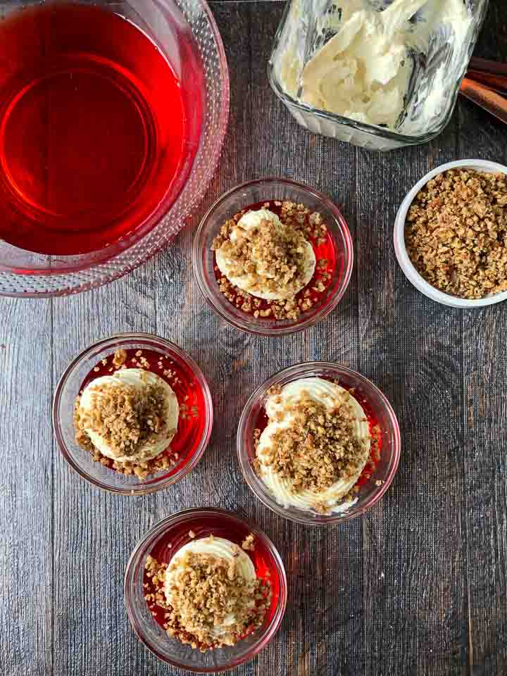 glass cups with keto strawberry jello desserst  and a bowl of strawberry jello, glass cup of cheesecake filling and a dish of crushed nuts