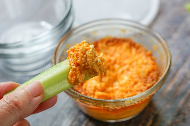 fingers holding a piece of celery dipped in the microwave keto buffalo chicken dip