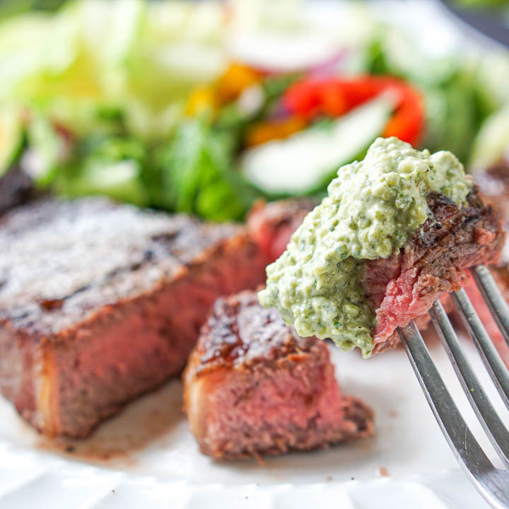 closeup of a piece of steak on a fork dipped in a creamy grilled poblano sauce with the rest of the steak in the background