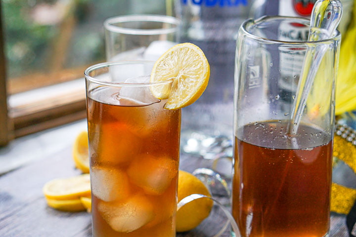 tall glass and pitcher filled with Long Island ice teas and bottles of alcohol in the background