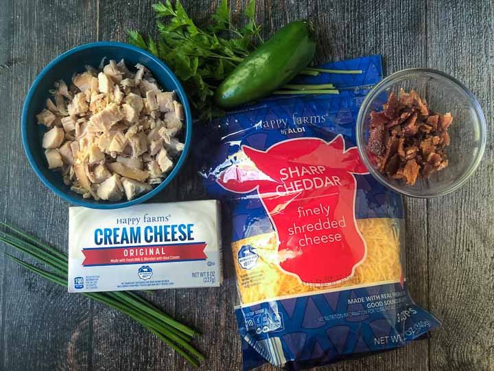 ingredients to make a buffalo chicken cheeseball: chopped cooked chicken, jalapeno, cheddar cheese, cream cheese, chives and crumbled bacon