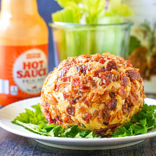 white plate with keto buffalo chicken cheeseball with a bottle of hot sauce and celery sticks in the background