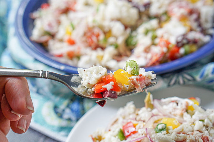 closeup of a forkful of low carb antipasto cauliflower rice salad with blue bowl in background