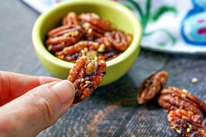 fingers holding a spiced pecan with a little green bowl in the background