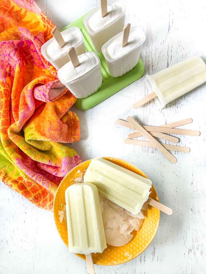 yellow bowl with 2 keto pina colada pops and a green popsicle mold with 4 more and scattered popsicle sticks