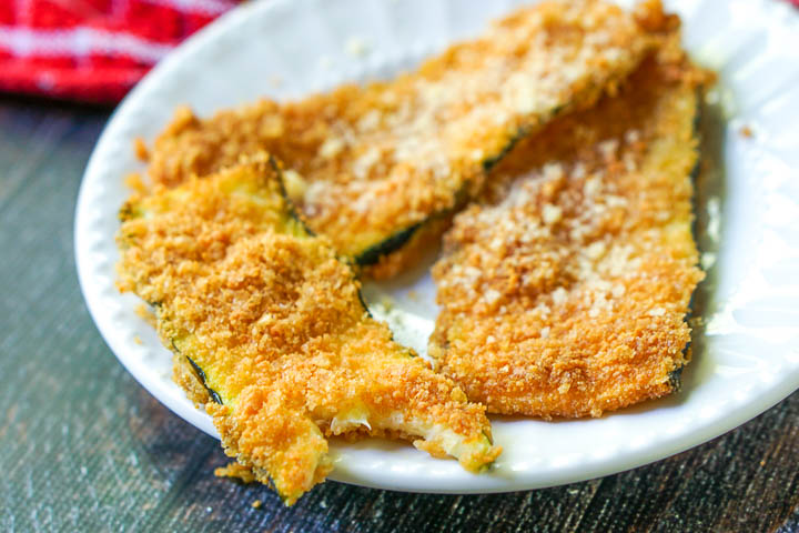 closeup of a white plate with a piece of fried zucchini with a bite taken out.