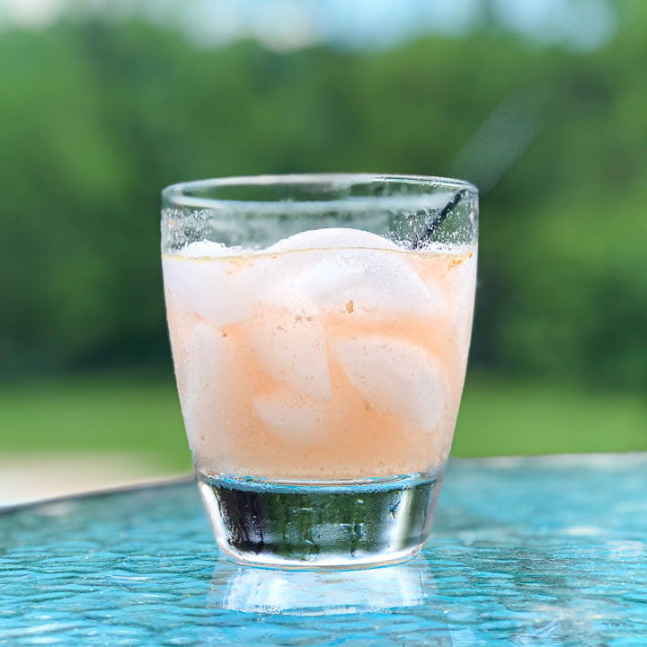 glass with ginger peach mule on a glass table out side with trees in background