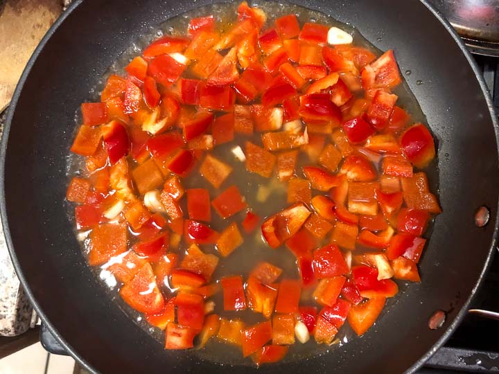 skillet with chunks of red pepper and garlic in a chicken broth