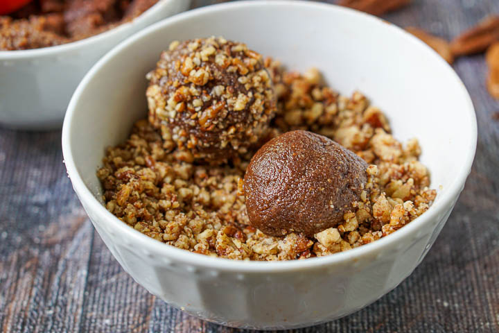 closeup of a white bowl with chopped toasted pecans and one covered and another uncovered pecan pie balls