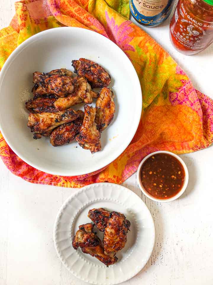 white bowl and plate with air fryer chicken wings and a bowl of Asian sauce and a colorful tea towel