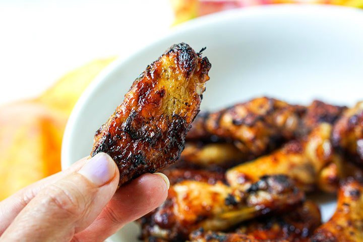 fingers holding 1 keto chicken wing with the bowl in the background