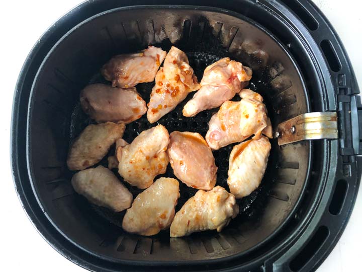 air fryer basket with frozen chicken wings based in Asian sauce