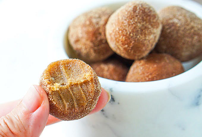 fingers holding the cinnamon sugar cookie dough ball with a bite taken out