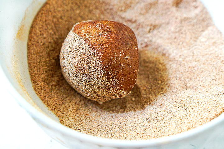 closeup of a bowl of cinnamon sugar with a fat bomb half rolled in