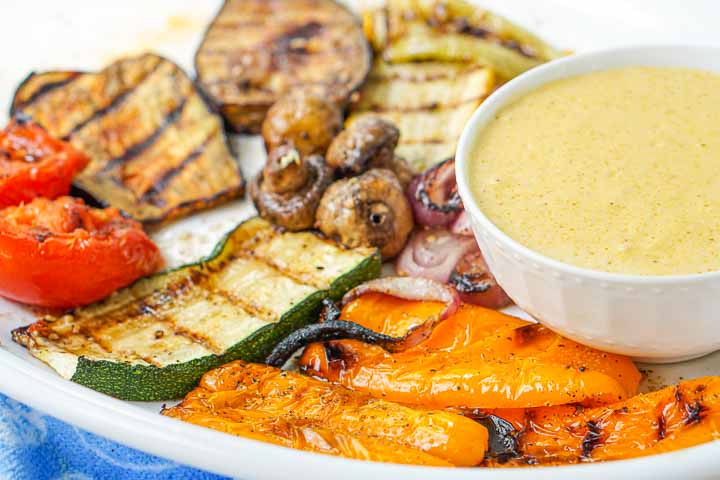 closeup of the platter of grilled vegetable with a bowl of garlic tahini sauce