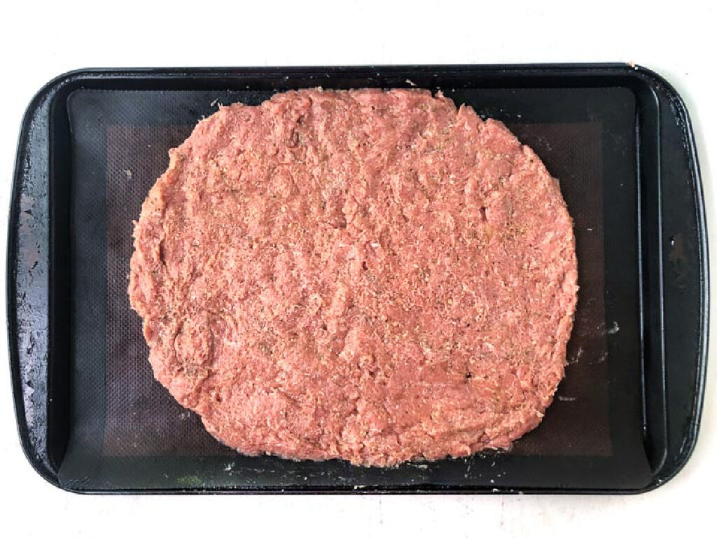baking tray with raw meat formed into a oval shape