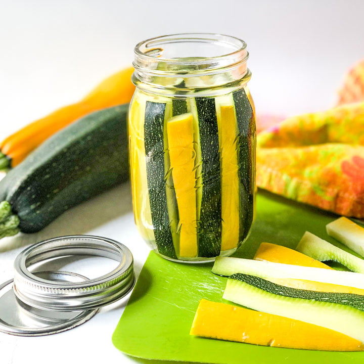 jar with yellow and green pickled zucchini spears with raw zucchini in the background