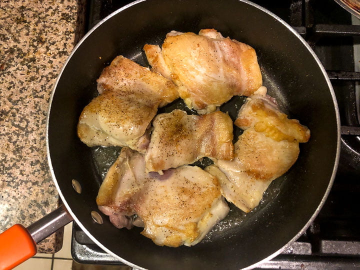 pan on the stove with browned boneless skinless chicken thighs