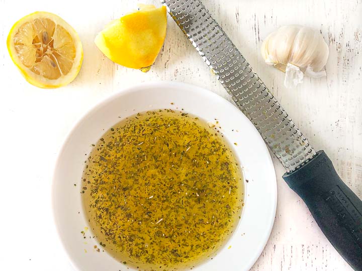 white bowl with Greek marinade a microplane, lemon halves and a head of garlic