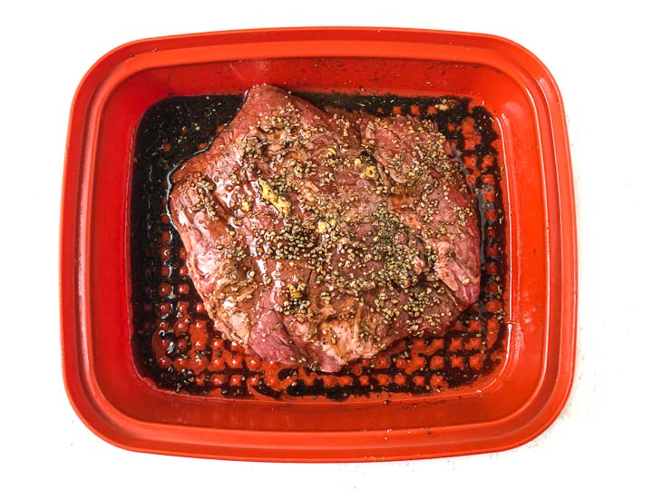 raw flank steak in a marinade in a large red orange container