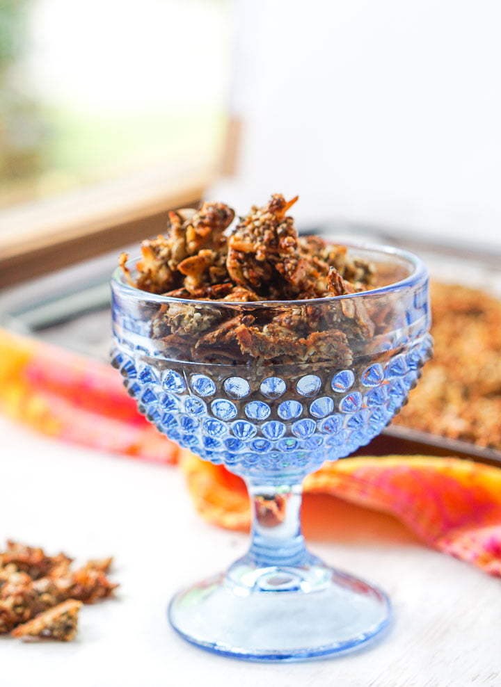 closeup blue glass dessert bowl with crunchy granola with a cookie sheet in the background