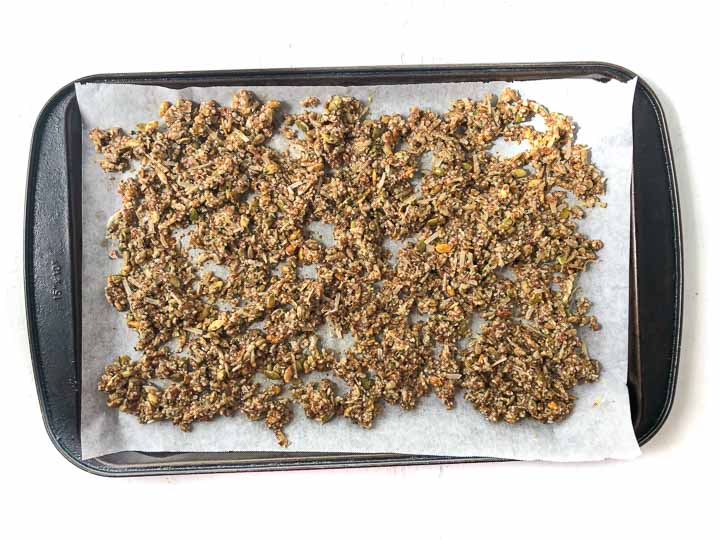 black cookie sheet with parchment paper and uncooked granola mixture