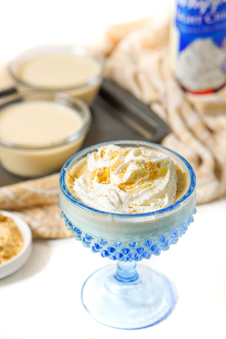 blue glass dessert dish with keto pudding with whipped cream and sprinkled pb powder on top. 