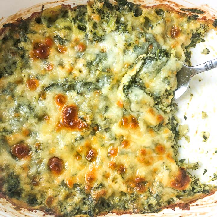 closeup of baking dish with keto spinach and broccoli cheese casserole with a spoon