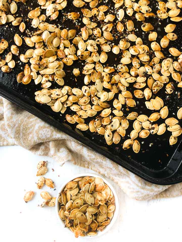 cookie sheet with roasted pumpkin seeds and a small white bowl with seeds