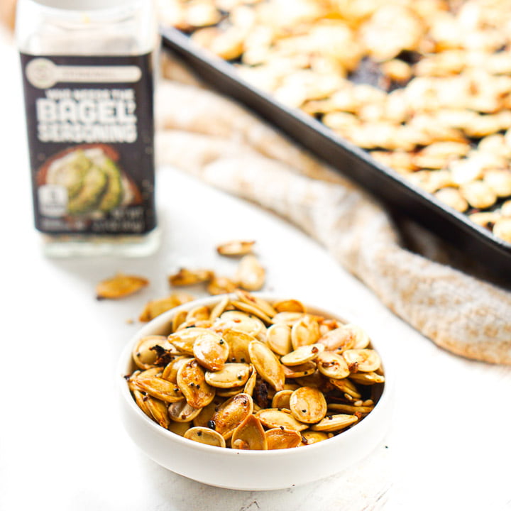 white bowl with low carb pumpkin seeds with a bottle of everything spice in background