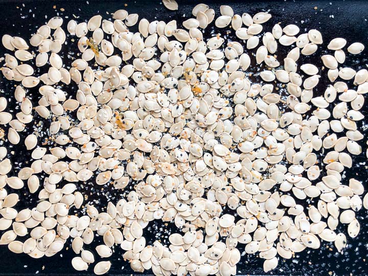 black cookie sheet with the scattered raw pumpkin seeds