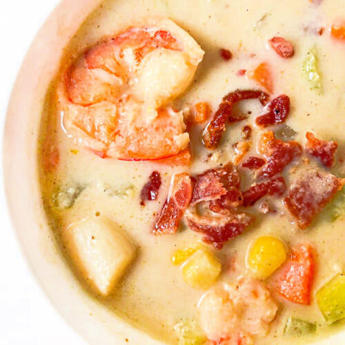 Closeup of a white bowl with keto seafood chowder with bacon crumbles on top.