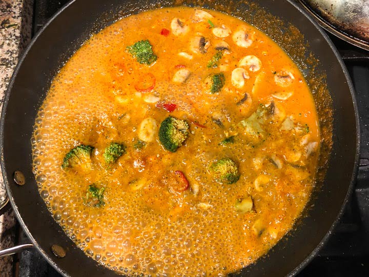 skillet with veggies and Thai curry sauce simmering