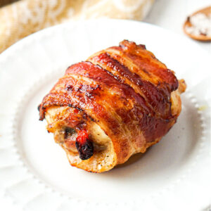 A white plate with a piece of bacon wrapped chicken thighs that were made in the air fryer.