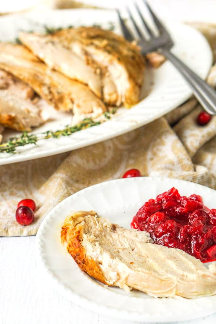 white plate with sliced instant pot turkey breast and cranberries with a turkey platter and fork in the background
