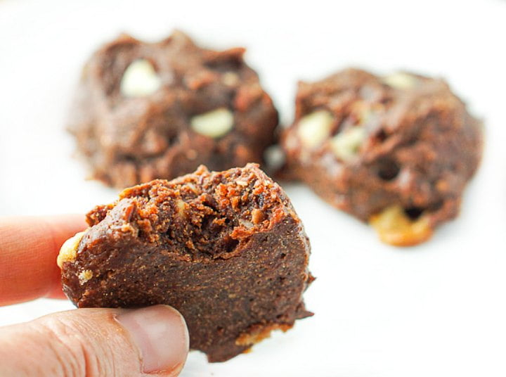 fingers holding a keto chocolate almond butter cookie with a bite taken o ut