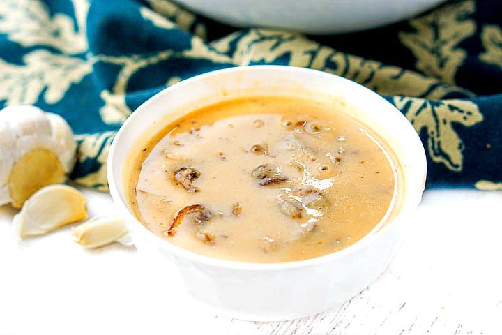 white bowl of savory low carb mushroom soup with garlic cloves beside