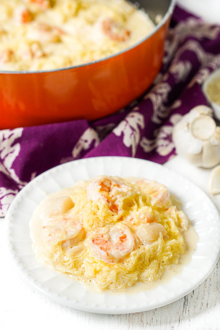 white plate with creamy spaghetti squash with shrimp and an orange pan in the background with a purple tea towel