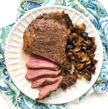 large ribeye steak sliced with garlic mushrooms on white plate