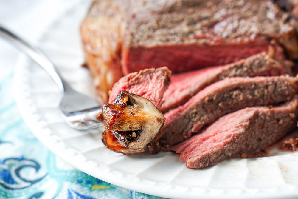 closeup of a piece of rare steak and a  browned mushroom on a fork