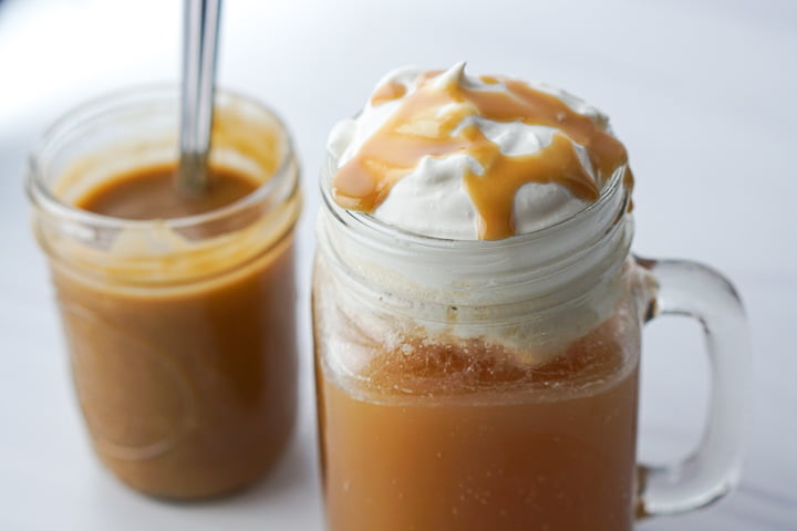 closeup of butter beer glass with butterscotch sauce drizzled on whipped topping and a jar of the sauce