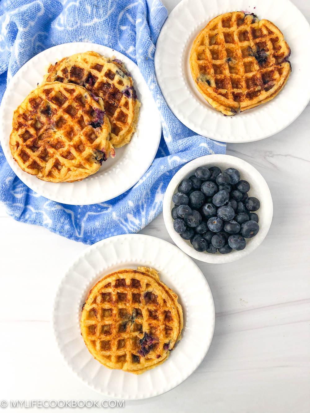 aerial view of 3 white plates with mini low carb blueberry waffles and a bowl of fresh blueberries