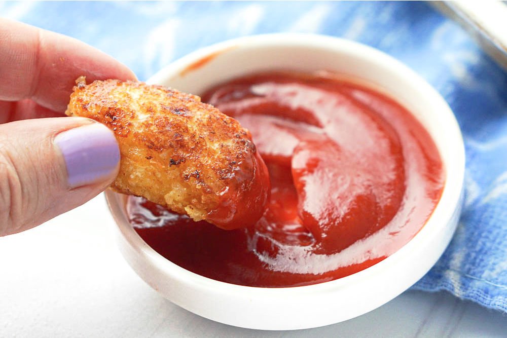 fingers holding a tot and dipping it in ketchup