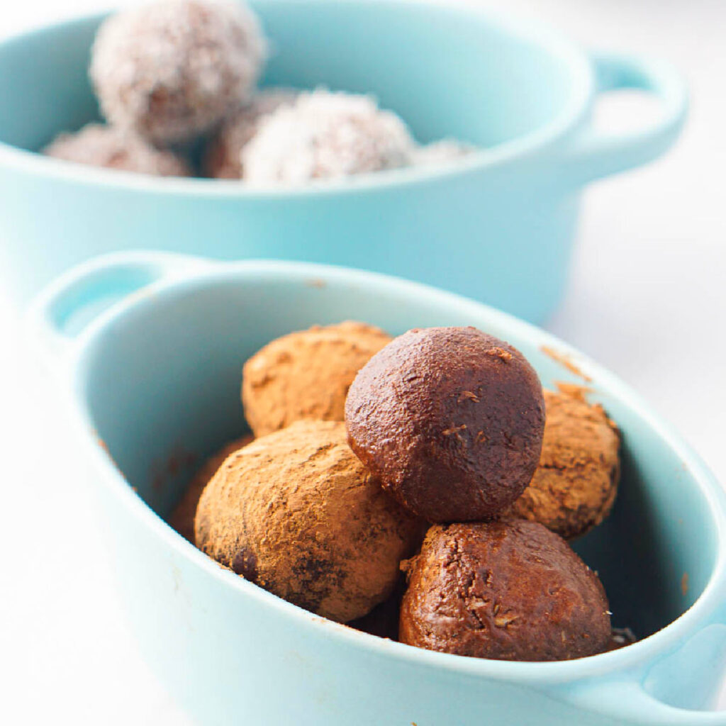 Low Carb Chocolate Coconut Protein Bites - only 0.5g net carbs per serving! The chocolate coconut keto protein balls in blue ceramic dishes.