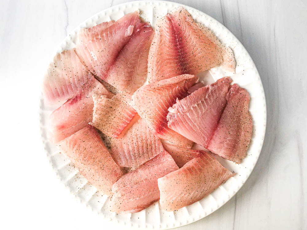 white plate with raw tilapia fillets cut in half