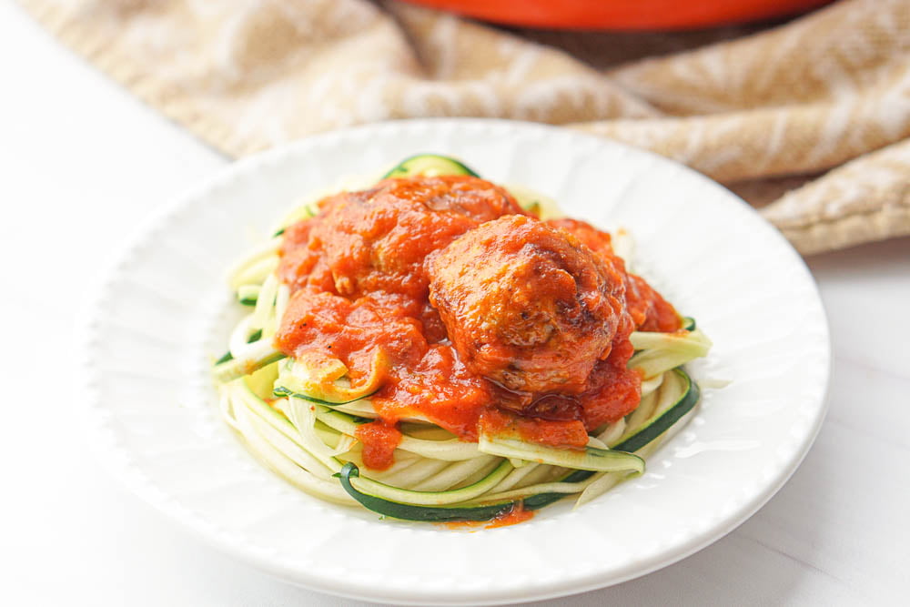 closeup of white plate with zucchini noodles topped with sauce and gluten free turkey meatballs