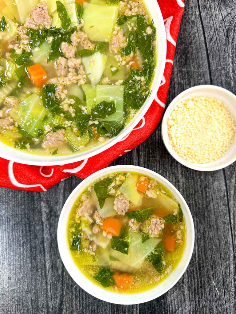 Aerial view of 2 white bowls with the low carb sausage and vegetables soup with parmesan cheese on the side.