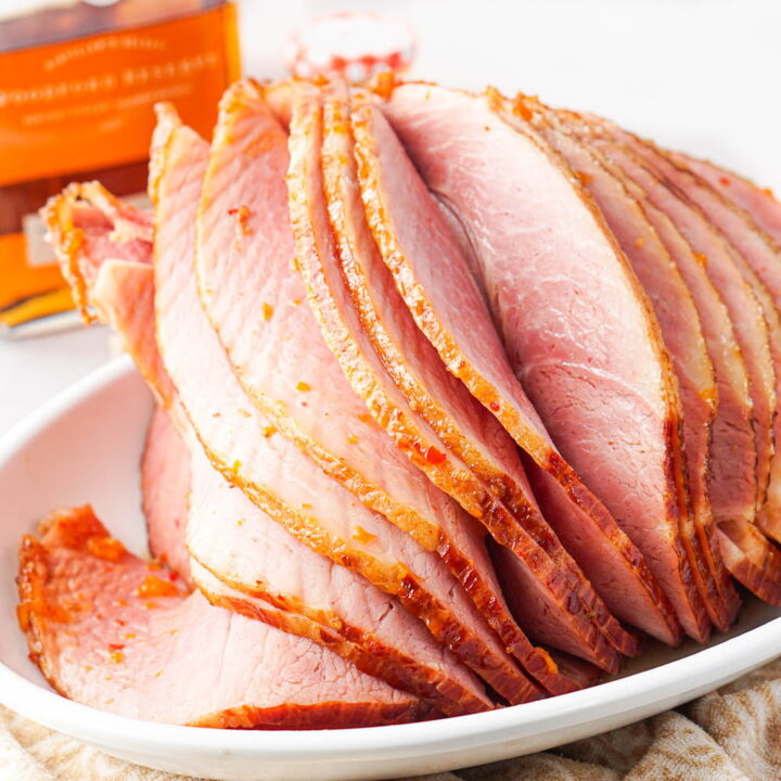closeup of an spiral cut glazed ham with a bottle of bourbon in the background